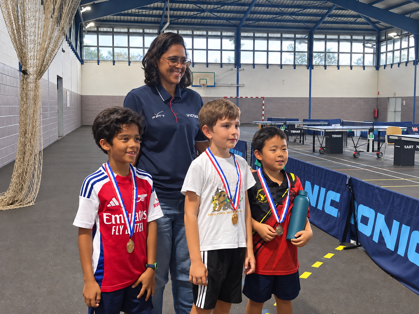Trois jeunes médaillés posent devant les tables de tennis de table