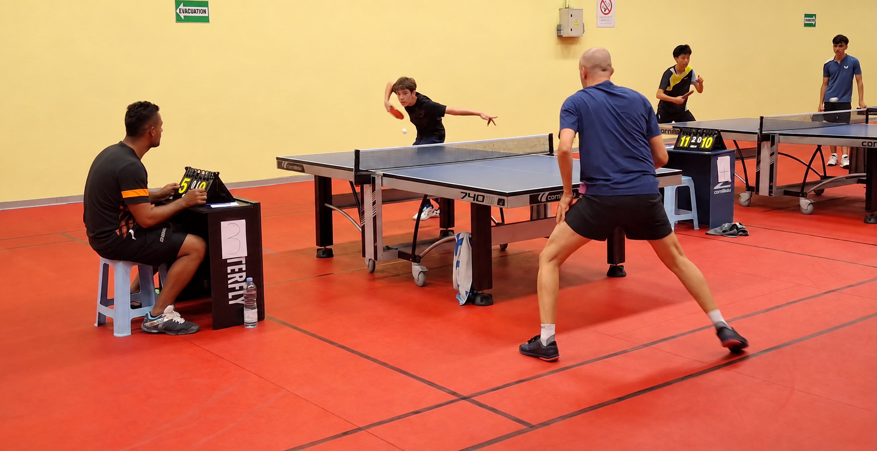 Plusieurs matchs de tennis de table disputés au gymnase des Deux Canons, avec un juge-arbitre au premier plan